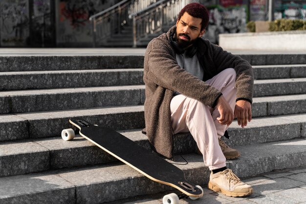 Tiro completo homem posando na escada com longboard