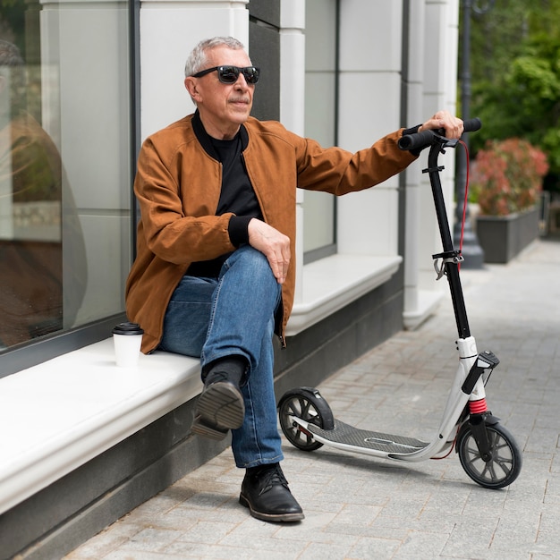 Tiro completo homem sentado ao ar livre com scooter