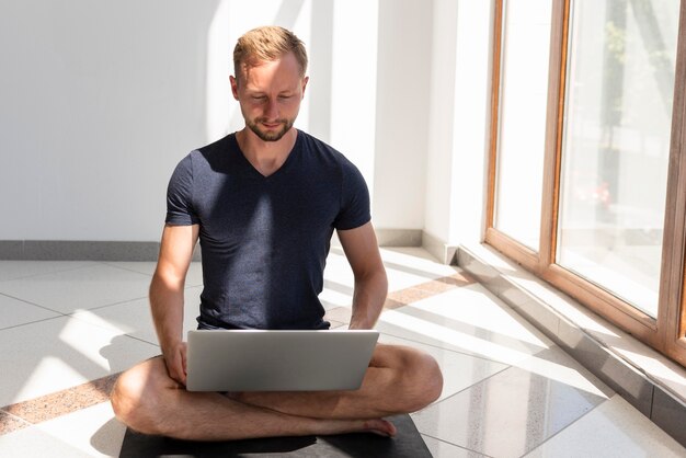 Tiro completo homem sentado na esteira de ioga e usando laptop