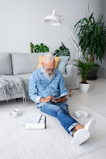 Foto grátis tiro completo homem sentado no chão com tablet