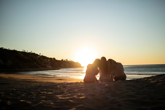 Tiro completo mulheres sentadas na praia ao pôr do sol