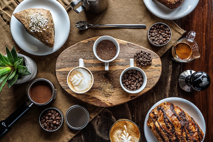 Foto grátis tiro de alto ângulo de grãos de café em potes em uma mesa de café da manhã com alguns bolos