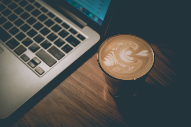 Tiro de ângulo alto de um copo de café ao lado de um laptop