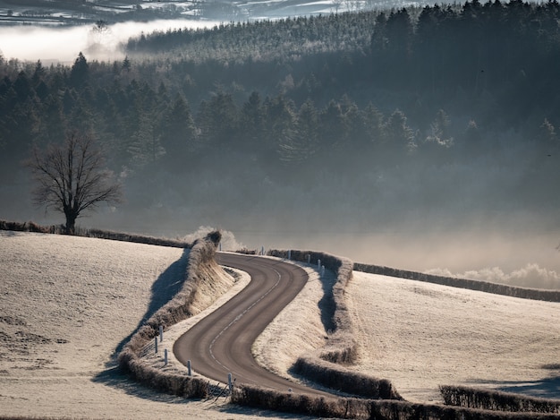 Tiro de ângulo alto de uma estrada curvilínea no meio de campos nevados com colinas arborizadas