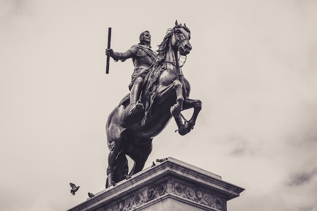 Tiro de ângulo baixo em escala de cinza de uma estátua em frente ao palácio real de madrid