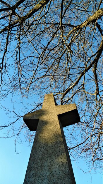 Tiro de ângulo baixo vertical de pedra feita cruz estátua com galhos e céu claro