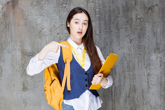 Tiro de menina bonita com pasta amarela em pé e posando. Foto de alta qualidade