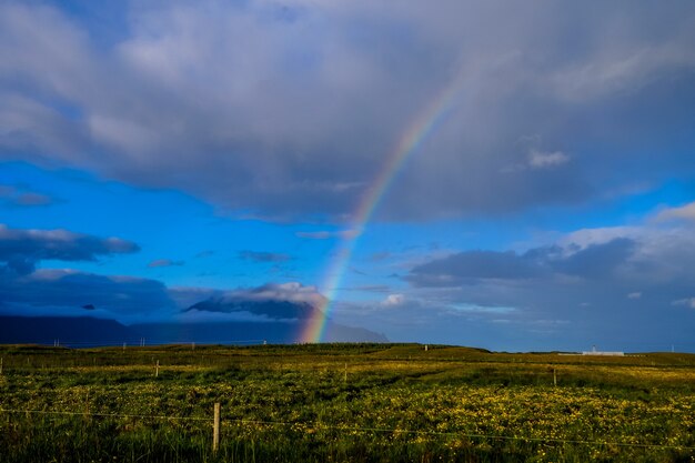 Tiro distante de um arco-íris sobre o horizonte acima de um campo de grama em um céu nublado
