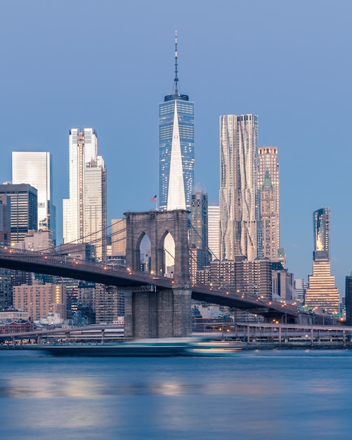 Tiro distante vertical da ponte do Brooklyn sobre o corpo de água perto de arranha-céus em Nova York