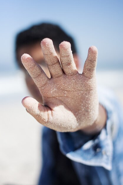 Tiro do close up do foco seletivo da palma arenosa de um homem que cobre sua cara na praia