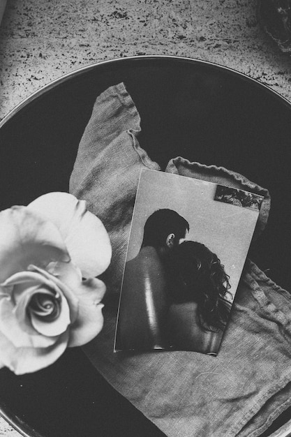 Tiro em escala de cinza vertical de uma fotografia de dois amantes ao lado de uma flor em um balde