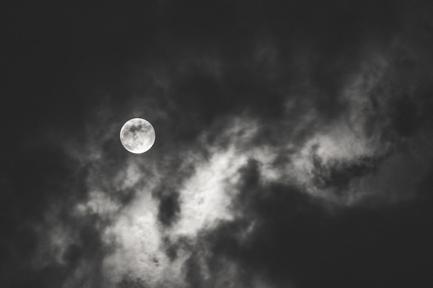 Foto grátis tiro escuro da lua cheia espalhando luz atrás das nuvens durante a noite