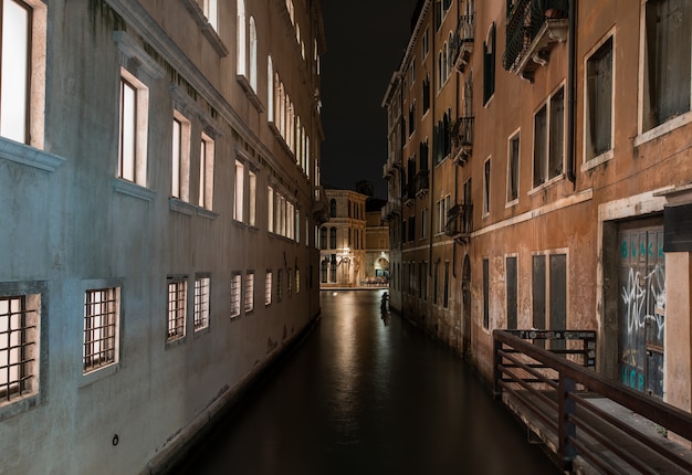 Tiro horizontal de um rio entre edifícios antigos, com belas texturas à noite em Veneza, Itália