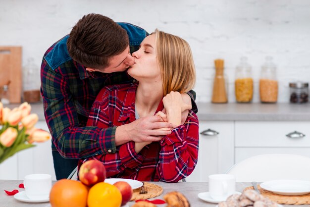 Tiro médio casal a beijar na cozinha