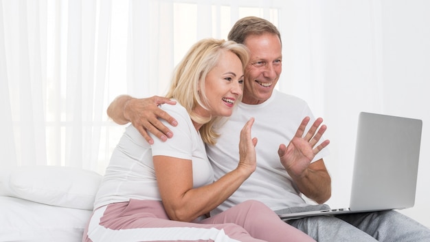 Tiro médio casal feliz com laptop acenando