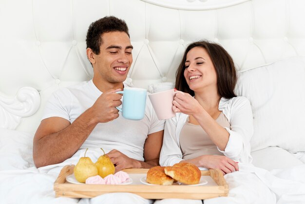 Tiro médio casal feliz tomando café da manhã na cama