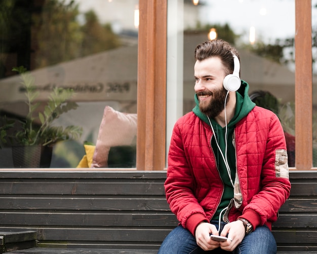 Tiro médio do smiley com fones de ouvido, sentado em um banco