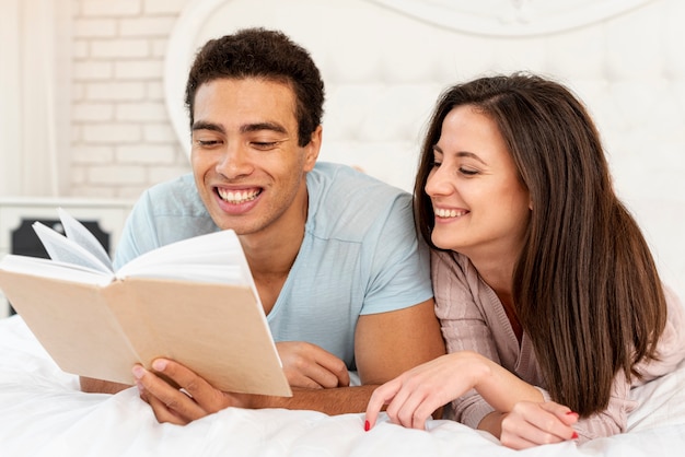 Tiro médio sorridente casal lendo na cama