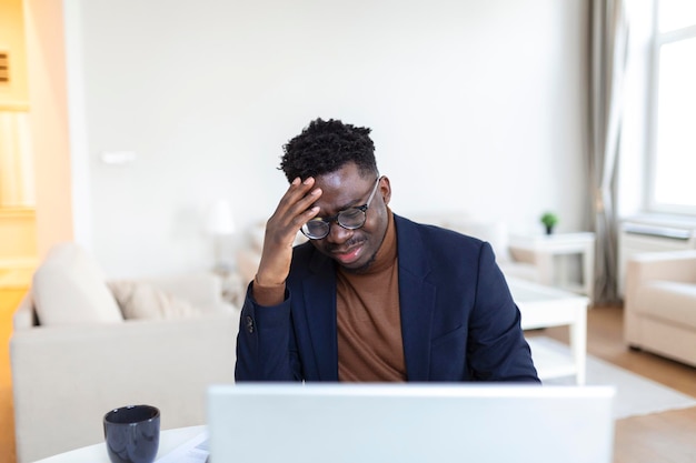 Tiro na cabeça estressado jovem afro-americano tocando a testa sofrendo de terrível dor de cabeça trabalhando no computador no escritório em casa Cara biracial confuso frustrado tendo sentimentos dolorosos na cabeça