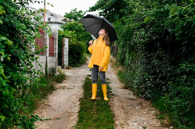 Tiro no escuro mulher em roupas de chuva, segurando um guarda-chuva