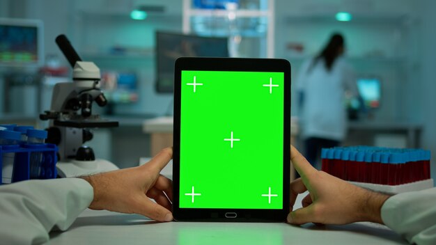 Tiro POV de químico usando tablet com tela verde em laboratório biológico. Trabalhador médico vestindo jaleco branco na clínica trabalhando com notebook com chroma key em exibição isolada em laboratório médico