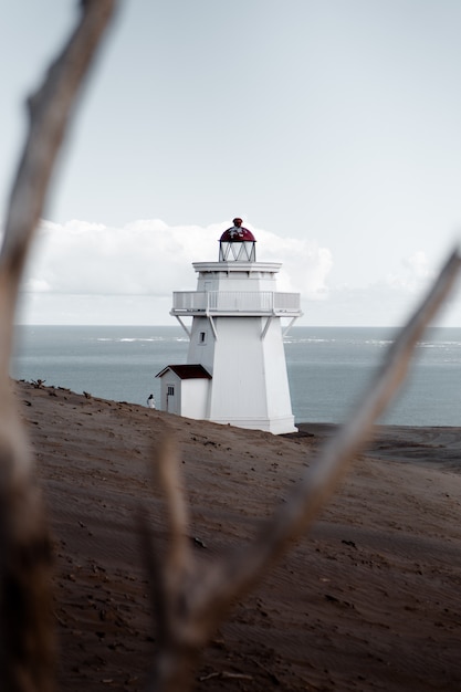 Foto grátis tiro seletivo vertical de um farol branco em uma praia arenosa