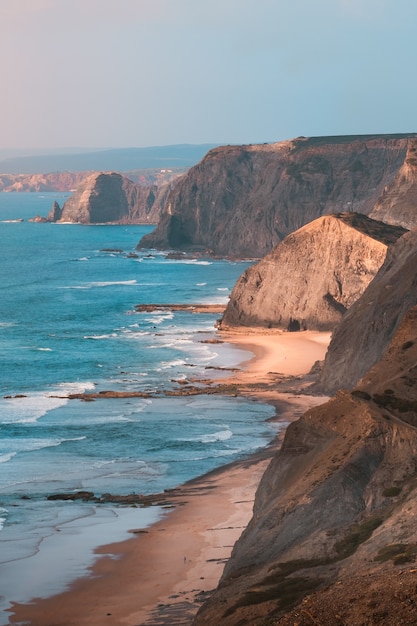 Foto grátis tiro vertical das belas falésias rochosas à beira-mar sob o incrível céu azul claro