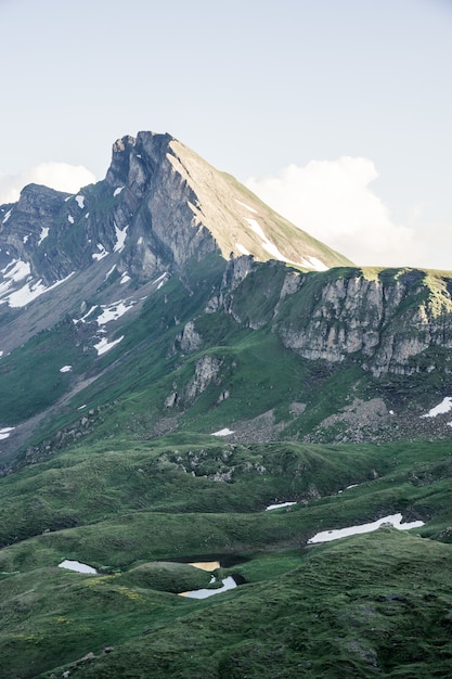 Tiro vertical de colinas gramadas perto de uma montanha com um céu claro ao fundo