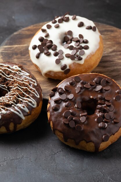 Tiro vertical de donuts vitrificados cobertos com lascas de chocolate em uma superfície rústica