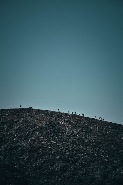 Foto grátis tiro vertical de pessoas andando em uma colina rochosa íngreme à distância