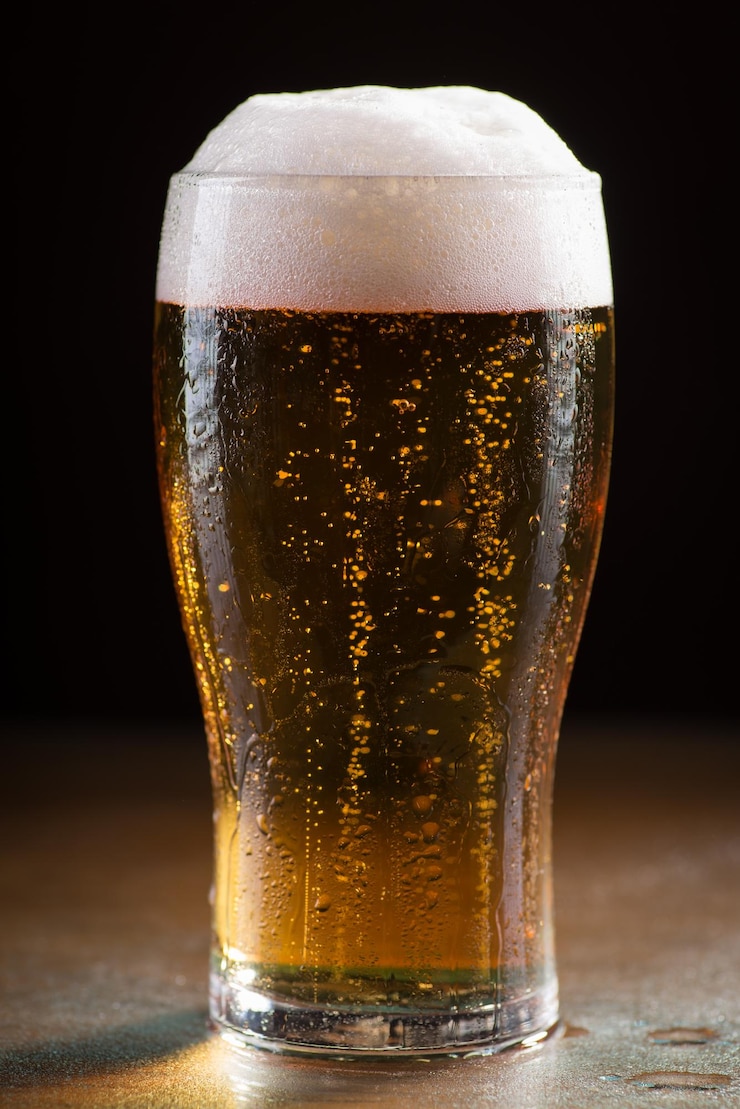 Foto grátis tiro vertical de um copo de cerveja gelada com espuma em uma mesa de madeira