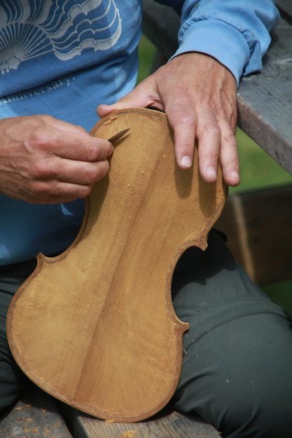 Foto grátis tiro vertical de um homem fazendo um violino de madeira no meio de um parque