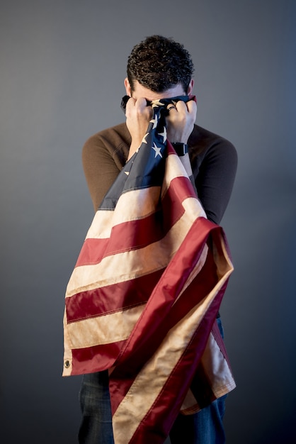 Tiro vertical de um soldado aposentado chorando de dor e limpando as lágrimas com a bandeira dos estados unidos