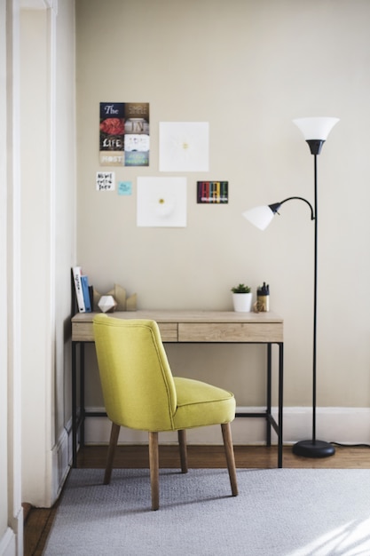 Tiro vertical de uma cadeira amarela e lâmpada alta perto de uma mesa de madeira com livros e vasos de plantas nele