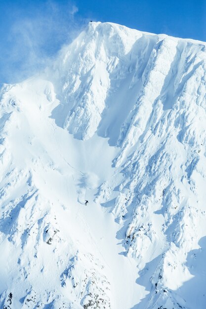 Tiro vertical de uma cordilheira alta coberta de neve sob o céu azul claro