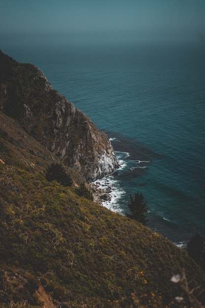 Tiro vertical de uma costa verde montanhosa e oceano azul com pedras