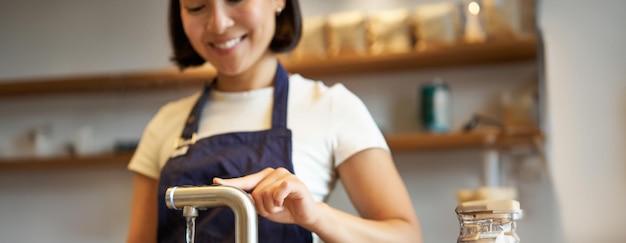 Tiro vertical de uma garota barista em um café derramando água da torneira usando uma chaleira para preparar café filtrado