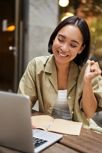 Tiro vertical de uma garota feliz falando em videochamada olha para laptop tendo reunião on-line sentado em o