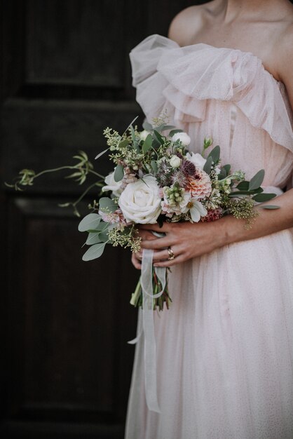 Tiro vertical de uma noiva usando vestido de noiva, segurando um buquê de flores