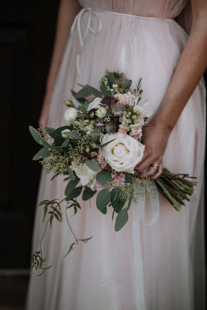 Foto grátis tiro vertical de uma noiva usando vestido de noiva, segurando um buquê de flores