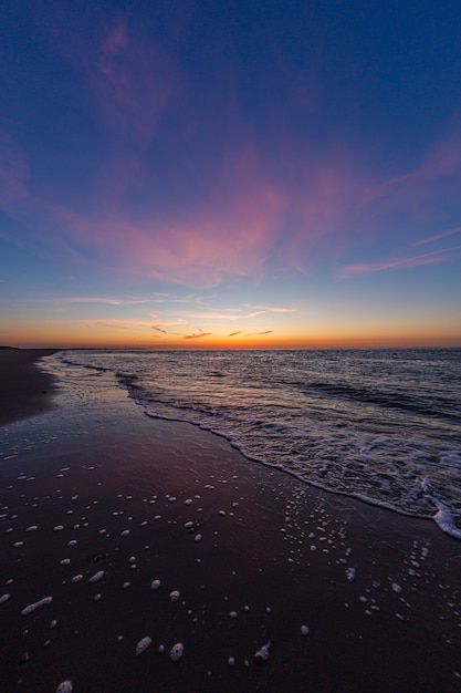 Foto grátis tiro vertical do oceano calmo durante o pôr do sol em vrouwenpolder, zeeland, holanda