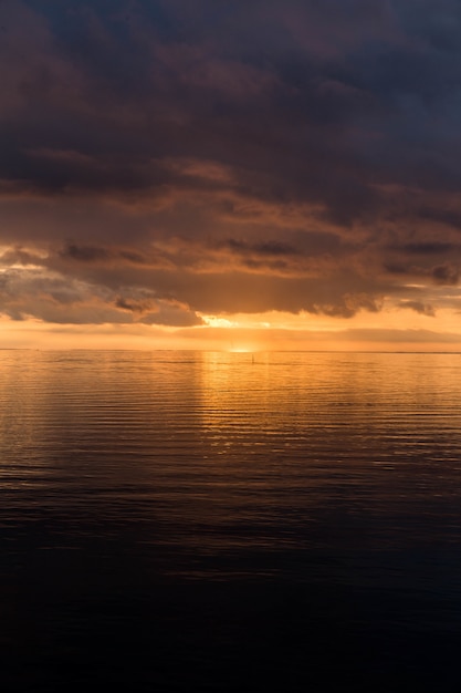 Tiro vertical do pôr do sol de tirar o fôlego no céu nublado sobre o oceano