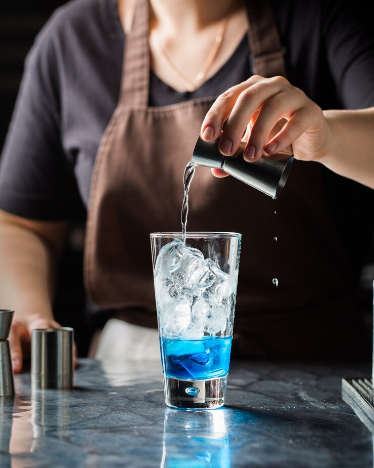 Foto grátis tiro vertical seletivo closeup de uma mulher fazendo bebida alcoólica azul com gelo