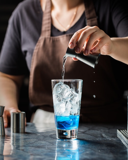 Tiro vertical seletivo closeup de uma mulher fazendo bebida alcoólica azul com gelo