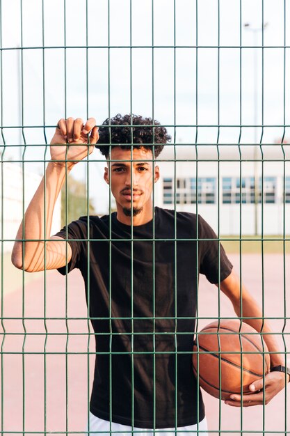 Étnica jovem macho com basquete por trás da cerca