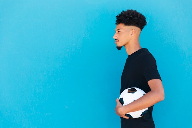 Étnico homem com cabelo encaracolado em pé com futebol