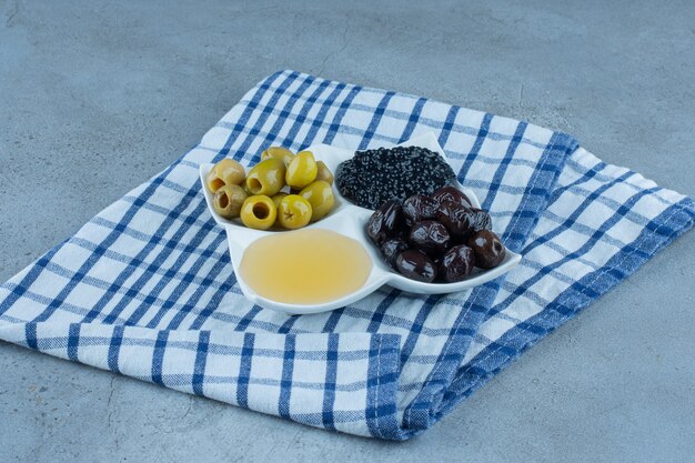 Toalha de mesa dobrada sob uma travessa de azeitonas sem caroço, mel e caviar em mármore.