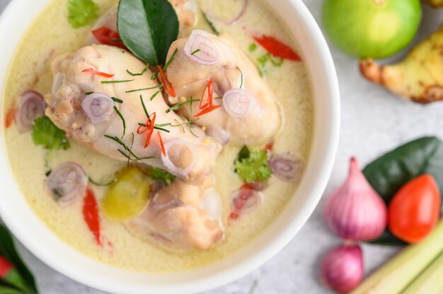 Tom Kha Kai em uma tigela com folhas de limão kaffir, erva-cidreira, cebola roxa, galanga e pimenta.