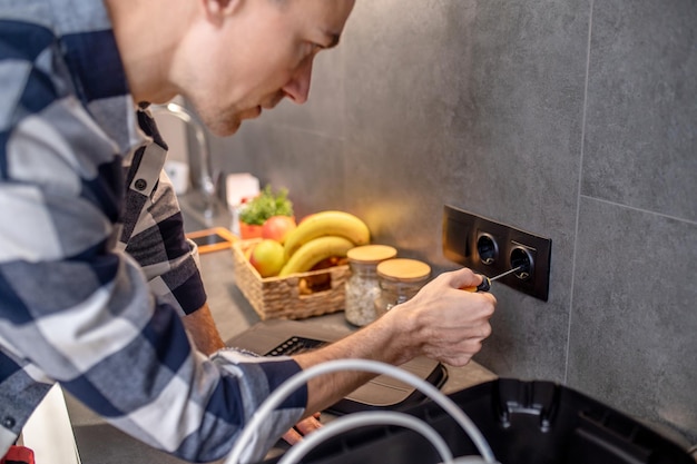 Foto grátis tomada de energia foto aproximada de homem tocando tomada preta na parede da cozinha com chave de fenda especial