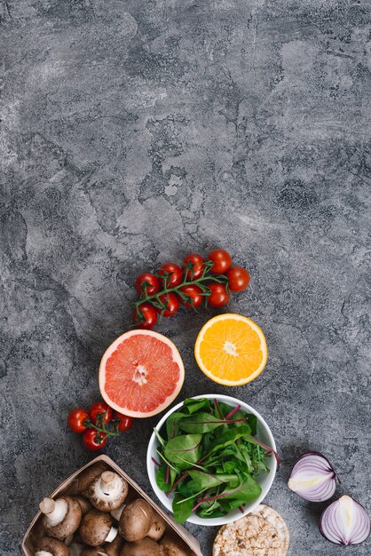 Tomate cereja; frutas cítricas cortadas ao meio; espinafre; cogumelos; cebola e arroz bolo tufado em pano de fundo concreto